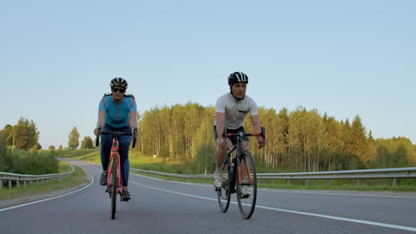 Dos-Ciclistas-Profesionales-De-Carretera-Andan-En-Bicicleta-Por-Una-Colina.-Toma-Manual-De-Dos-Ciclistas-Fuertes,-Femenino-Y-Masculino,-En-Su-Entrenamiento-En-Un-Cálido-Pero-Ventoso-Día-De-Verano.